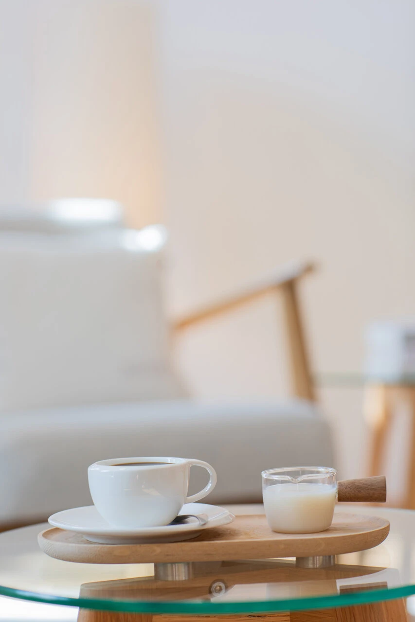 Eine Tasse Kaffee mit einem Milchkännchen am Couchtisch. im Hintergrund ein bequemer Lehnstuhl